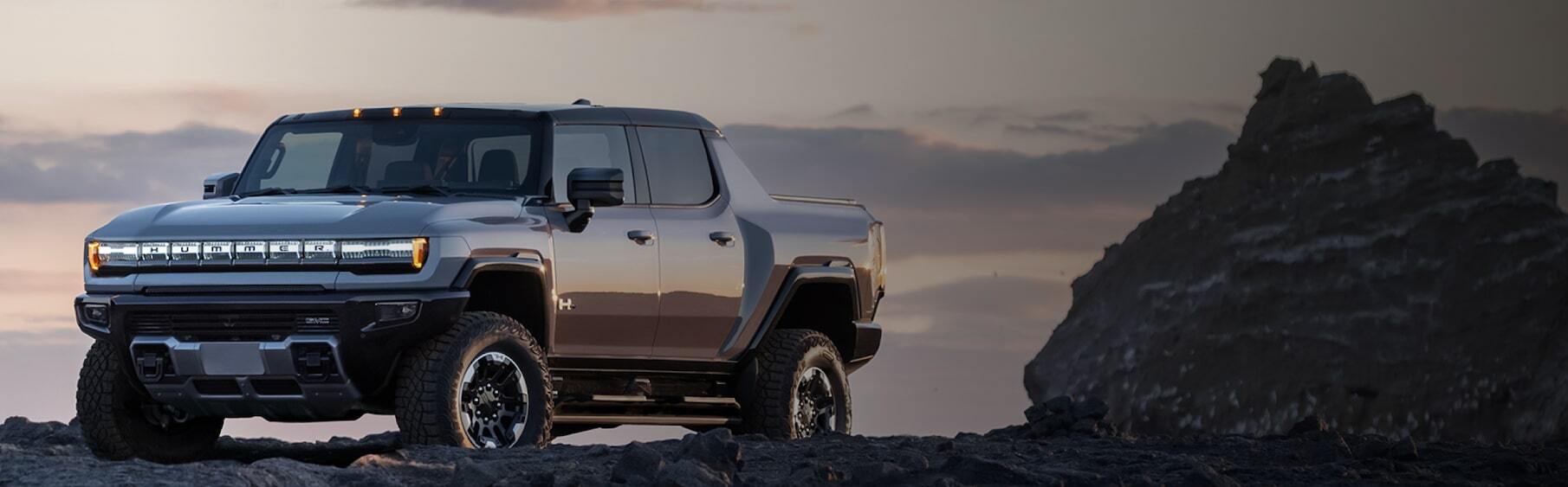 2026 GMC Hummer EV Pickup sitting on dirt terrain, sun setting in background